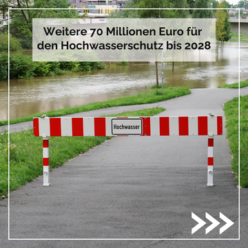 Absperrschranke "Hochwasser" für Weg, das zum Fluss führt, der die Wege überflutet. Text m Bild: Weitere 70 Millionen Euro für den Hochwasserschutz bis 2028