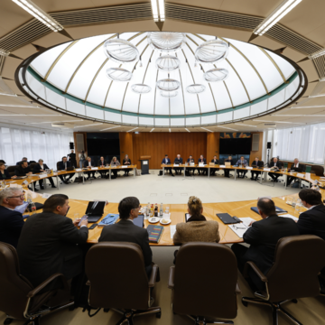 Das Foto zeigt die Teilnehmerinnen und Teilnehmer der Finanzministerkonferenz an einem runden Tisch im Konferenzraum mit Glaskuppel