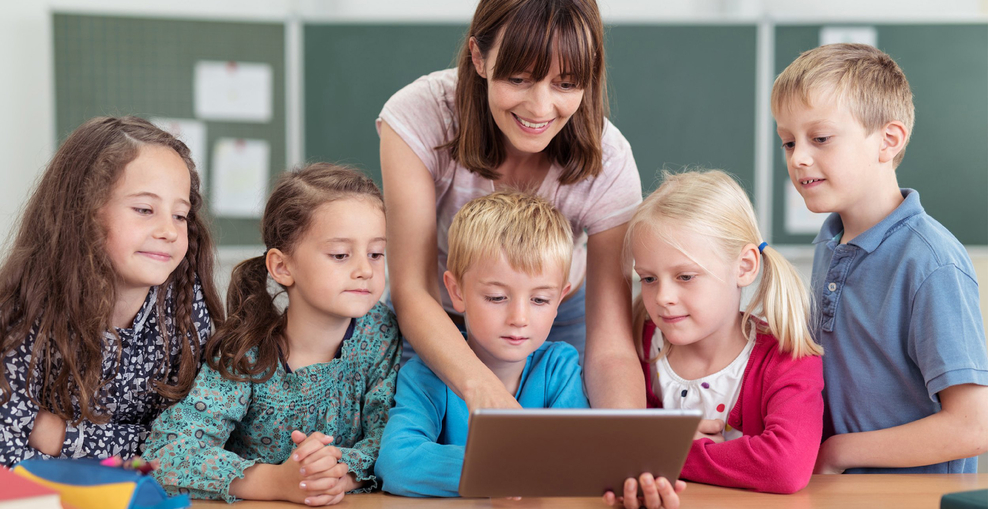 Lehrerin zeigt Kindern etwas am Tablet.